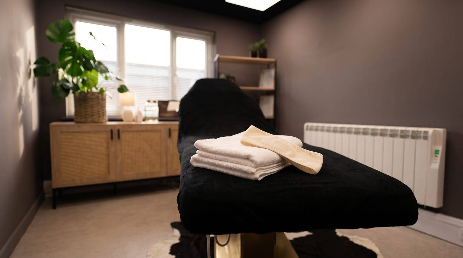 A neatly folded stack of clean white towels and a plain fabric headband set out ready on the treatment chair at Kennedy SMP Studio, Haverhill