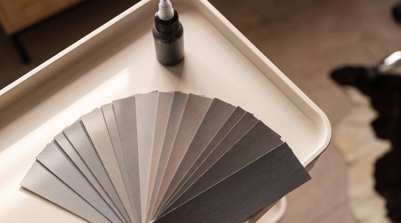 A fan of graded scalp micropigmentation pigment shade swatches, from soft grey through to deep charcoal, laid out on a tray beside an unbranded pigment bottle at Kennedy SMP Studio