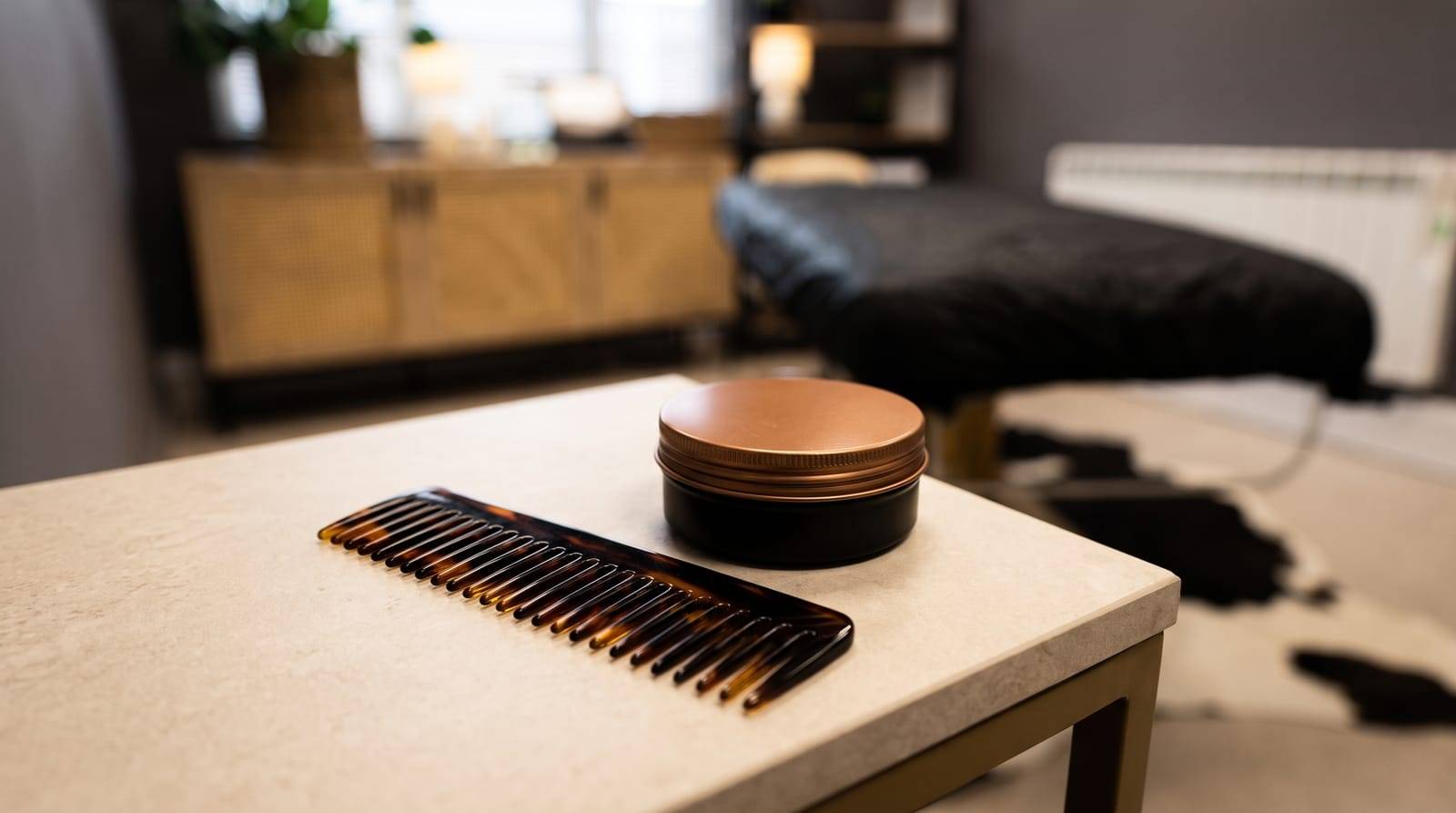 A comb and a small tin of styling product resting on a barbershop-style counter, the low-effort styling tools behind a good short cut