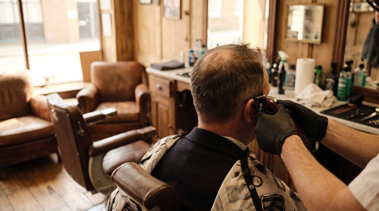 A short, textured haircut being clipped for thinning hair, seen from behind in a barbershop, no face in frame