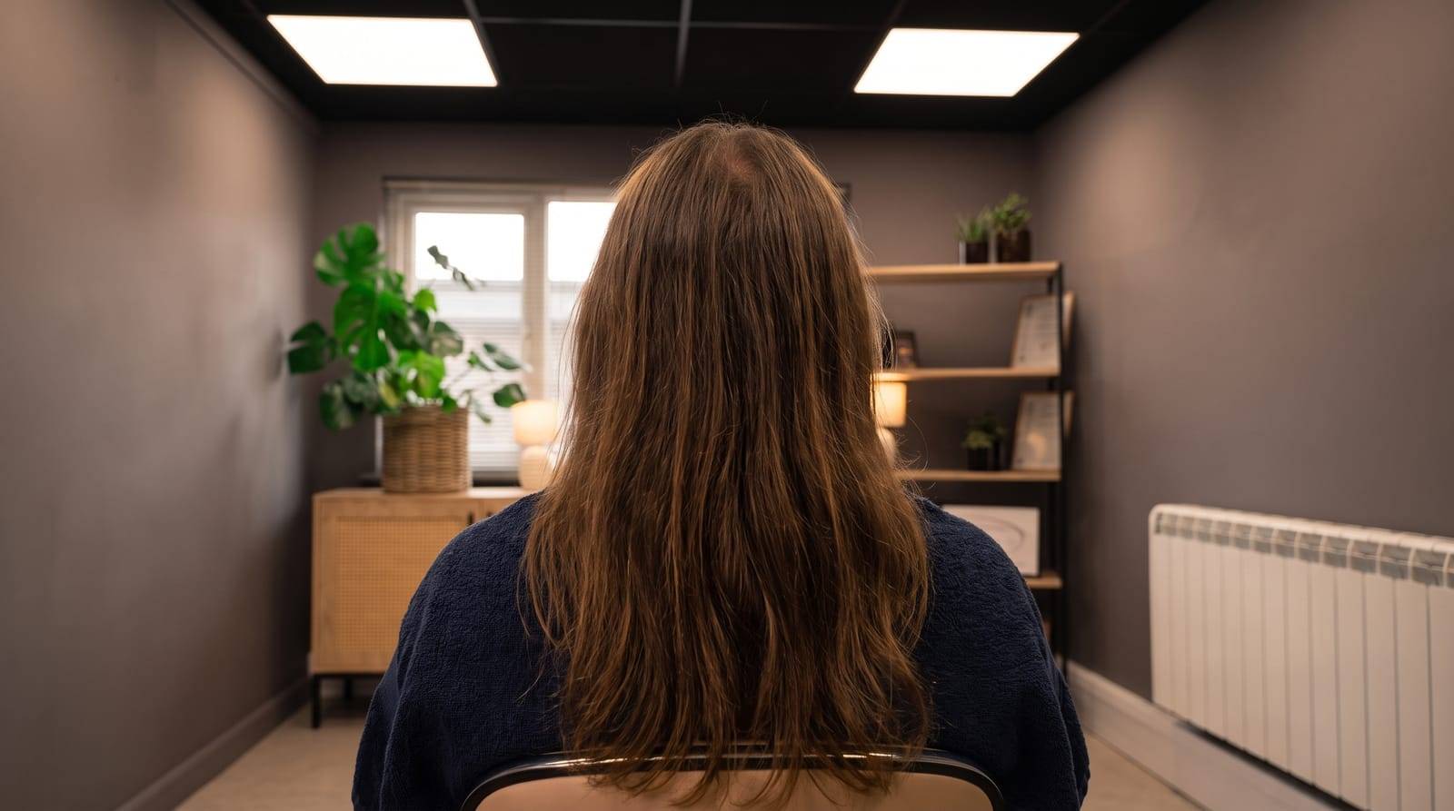 A person with long hair settling into the reclined treatment chair at Kennedy SMP Studio in Haverhill, ready for a consultation about density SMP